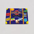 A rectangular luggage label print featuring a dark blue suitcase design with orange straps, yellow corner accents, and multiple colorful travel ticket graphics. The center reads “LUGGAGE LABELS” and “Bonjour Paris,” shown on a light gray background.