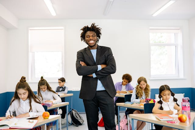 A teacher in a classroom smiling while students read books