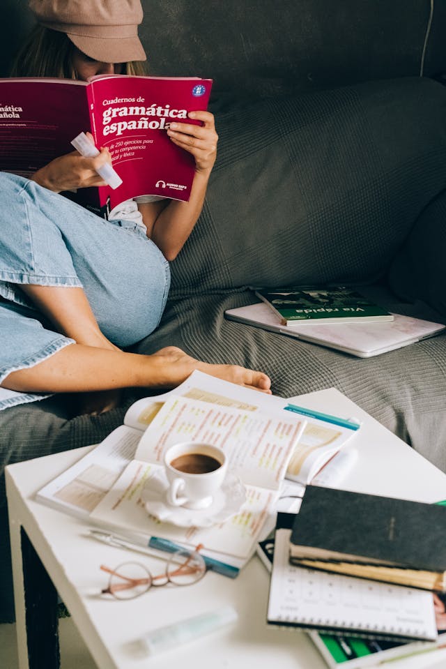 Woman studying a Spanish grammar book with notes and a coffee cup before her
