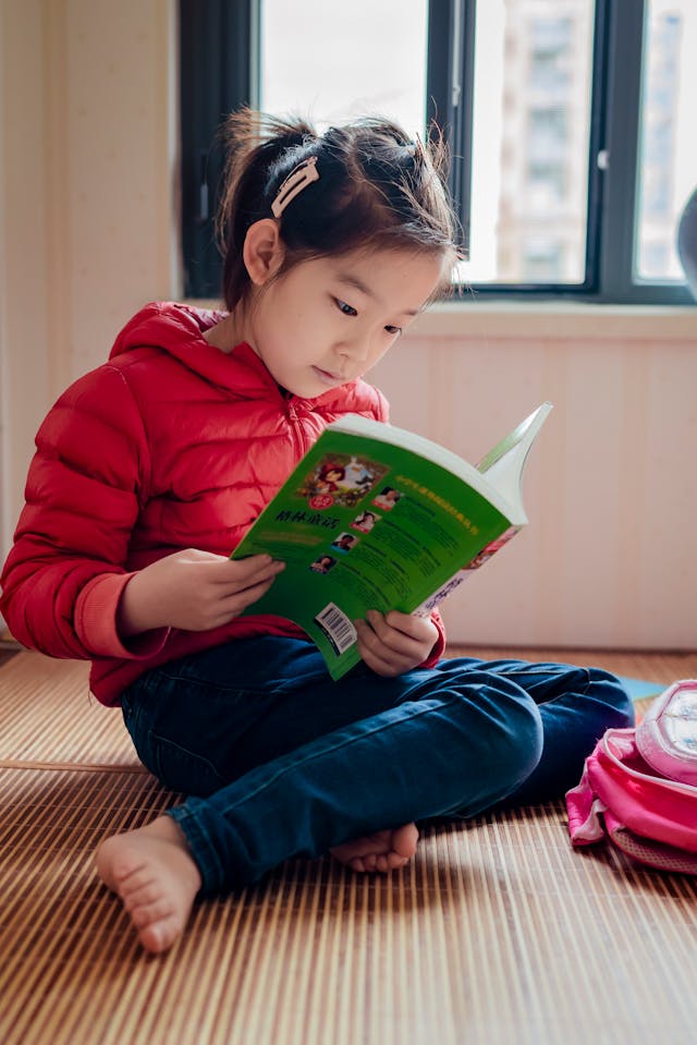 Young girl in a red jacket reading a green book